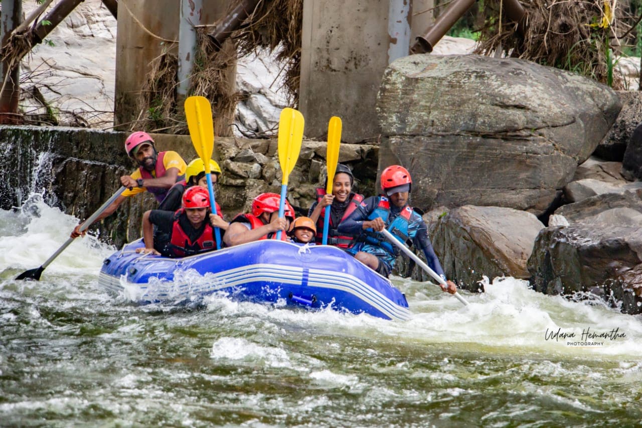 A raft crew raising their paddles in celebration after clearing a rapid on the Kelani River