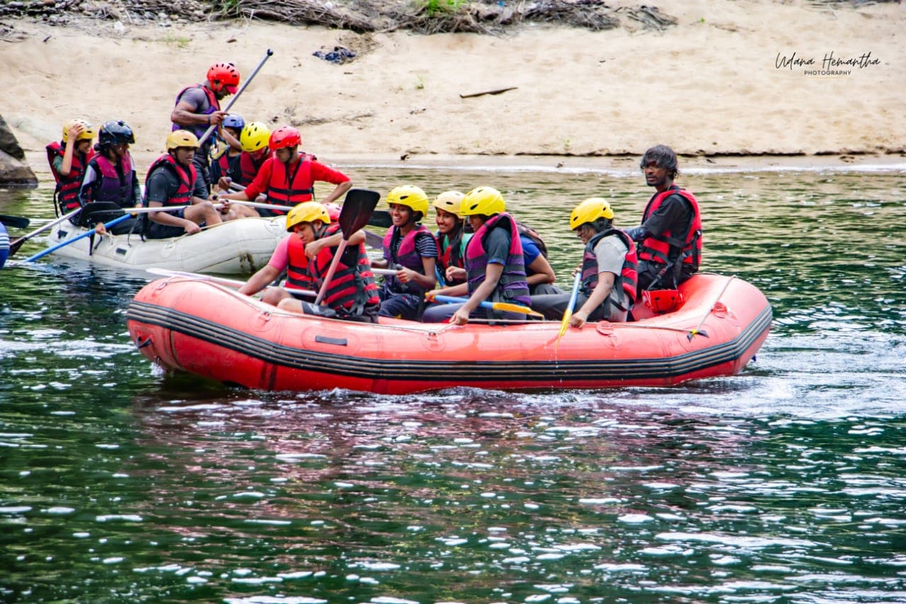 A student group in matching helmets and buoyancy aids stepping off their raft onto the sand beside the Kelani River at Kitulgala