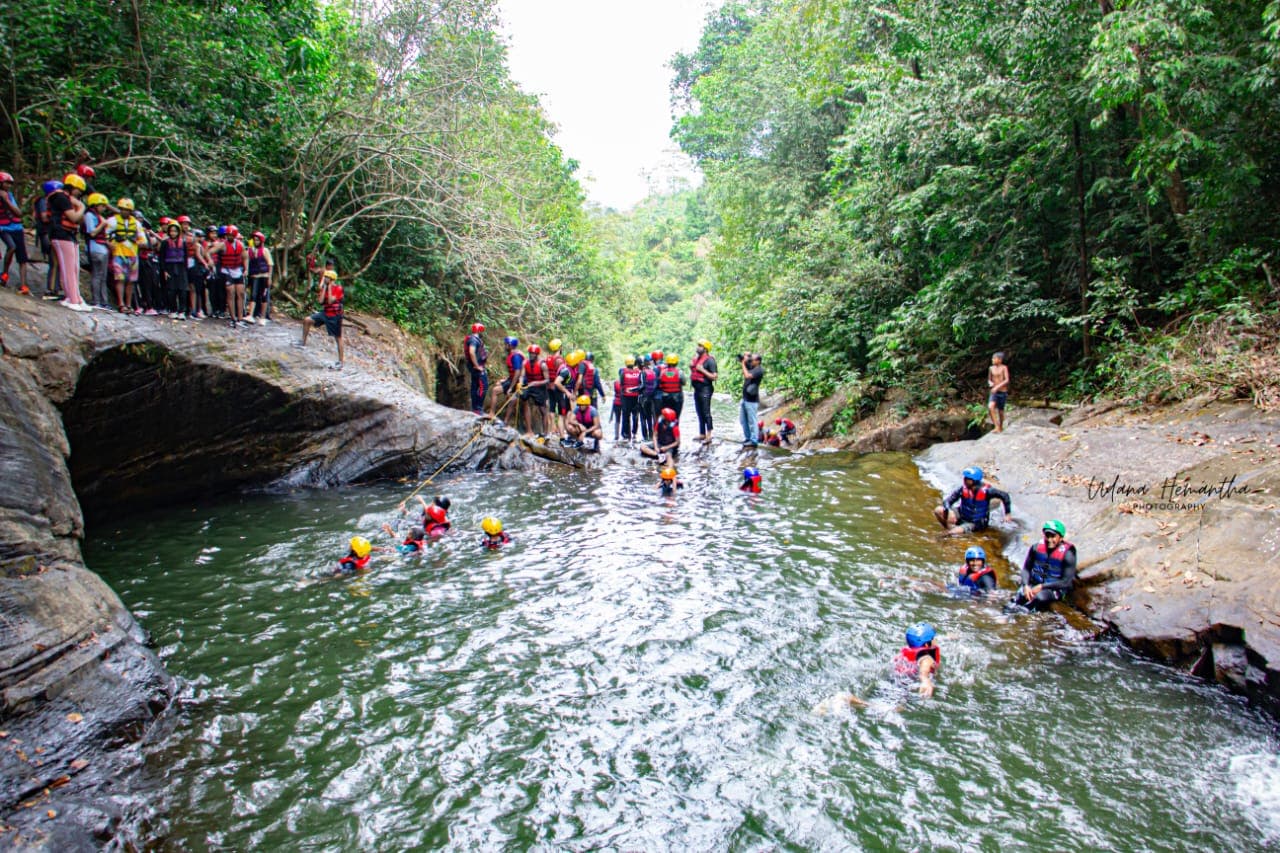 A large group spread through a rainforest gorge on a Kitulgala canyoning route, showing the scale of the natural setting