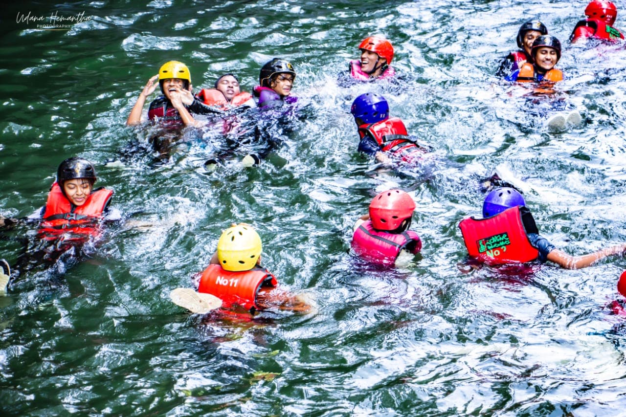 A student group swimming together in the Kelani River wearing numbered helmets and buoyancy aids for headcount checks