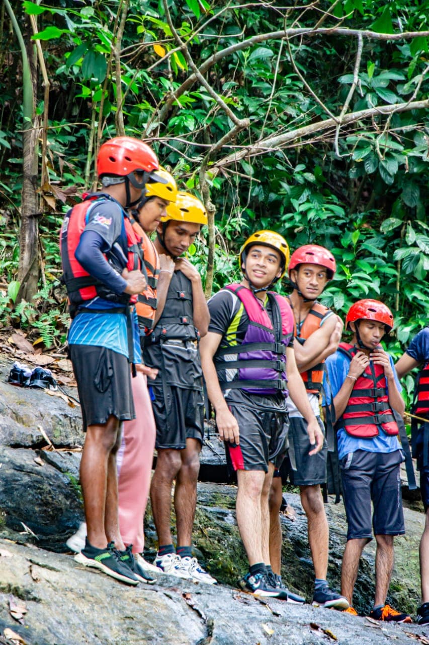 Members of a group helping each other fasten helmets and buoyancy aids on the rocks before a Kitulgala canyoning session