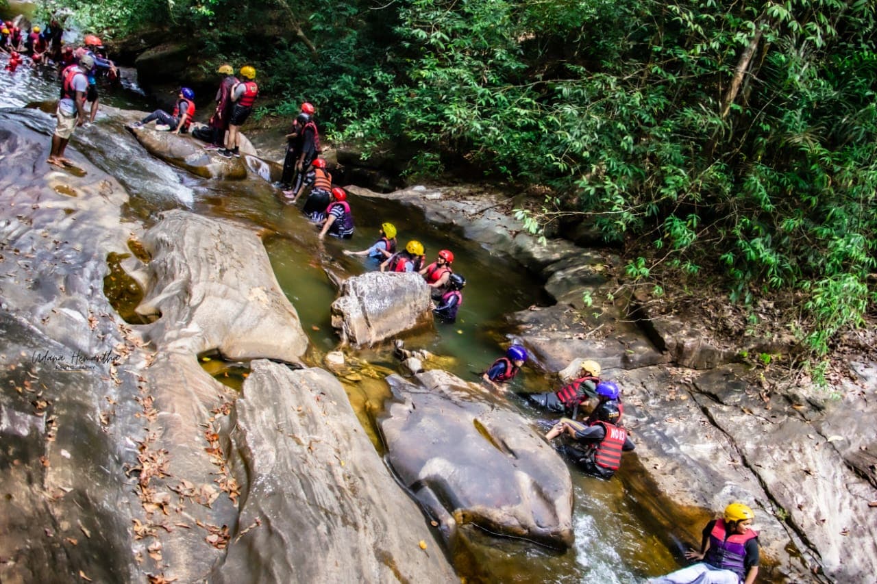 A group of around nineteen people making their way in single file up a canyoning stream in the Kitulgala rainforest
