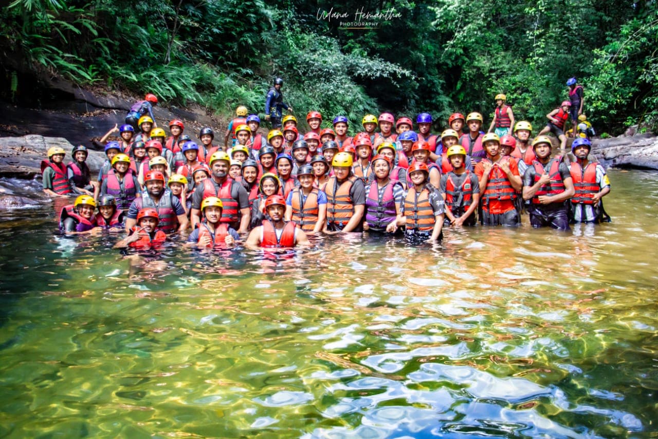 A company group of around fifty colleagues standing together in the Kelani River at Kitulgala after their Xclusive Adventures team building day